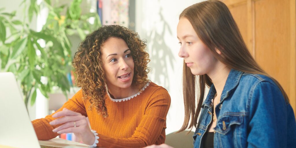Two women discussing insurance options at a laptop in a bright office; adviser explaining ways to manage rising premiums.