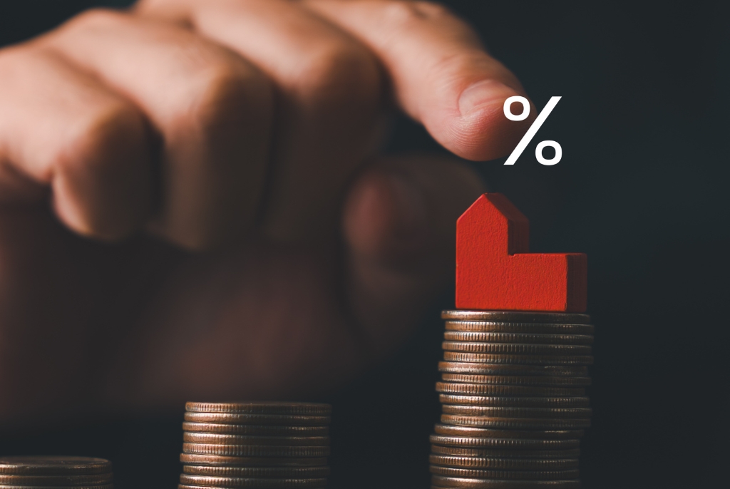 Stacked coins with a red house and percentage symbol, representing rising interest rates impacting business costs and insurance considerations.