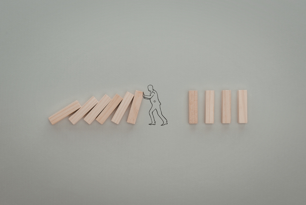 Domino blocks falling with a figure stopping the chain reaction, representing risk management and preventing business interruption losses.
