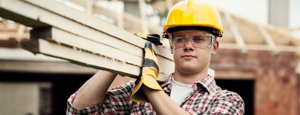 Owner builder carrying timber on a residential construction site wearing safety gear and owner builder insurance protection